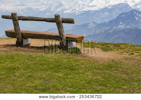 Wooden Bench On Green Grass With View Of Snow On Peak Of High Mountain, Rigi Kulm Luzern Switzerland
