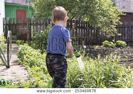 A Child In The Garden Watering Flowers, A Little Boy With A Water Hose Watering The Garden