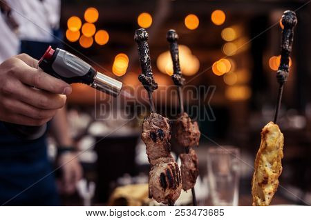 Meat On Skewer Fry With A Cooking Gas Torch Flomber. Preparation Of Delicious Fresh Meat Frying With