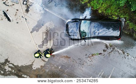 Two Firefighters Extinguishing A Burning Car After An Accident.