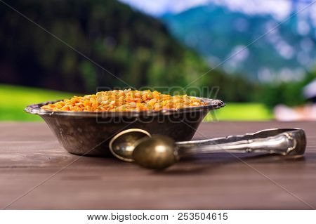 Lot Of Whole Raw Red Lentils And Sugar Tongs In Old Iron Bowl With Country Nature In Background