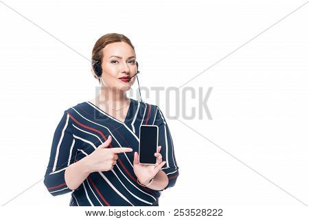 Female Operator Of Call Center With Headset Pointing At Smartphone With Blank Screen Isolated On Whi