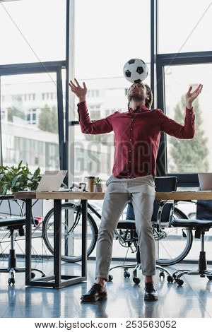 Low Angle View Of Young Businessman Balancing Soccer Ball On Head In Office