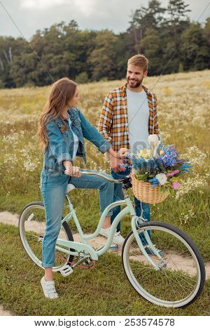 Smiling Young Lovers With Retro Bicycle In Field With Wild Flowers