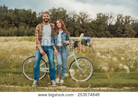 Young Lovers With Retro Bicycle In Field With Wild Flowers