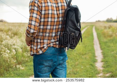 Partial View Of Man In Jeans With Black Leather Backpack Standing In Field