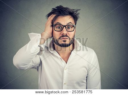 Young Lost And Dumbfounded Man With Hand On Head Wearing Glasses And Looking Perplexed At Camera On 