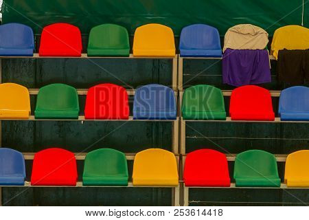 Multicolored Empty Plastic Chairs In The Stands Of The Stadium. Many Empty Seats For Spectators In T