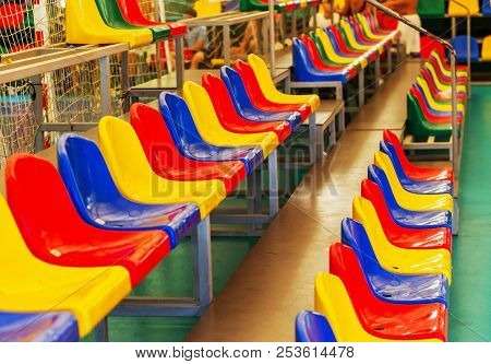 Multicolored Empty Plastic Chairs In The Stands Of The Stadium. Many Empty Seats For Spectators In T