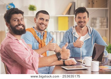 Three Young Smiling Men In Room With Laptop. Friendship Concept. Man Using Digital Device. Men With 