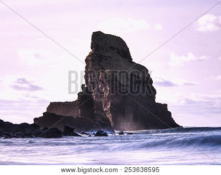 Sharp Silhouette Of A Cliff Against The Background Of Sunset. Sea Waves Break On The Rocks. Talisker