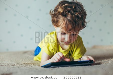 Little Cute Boy In A Green T-shirt Playing Games On A Tablet And Watching Cartoons. Addiction Concep