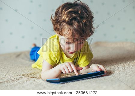 Little Cute Boy In A Green T-shirt Playing Games On A Tablet And Watching Cartoons. Addiction Concep
