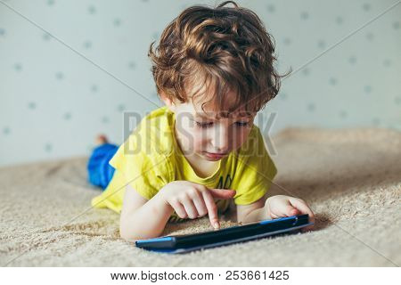 Little Cute Boy In A Green T-shirt Playing Games On A Tablet And Watching Cartoons. Addiction Concep