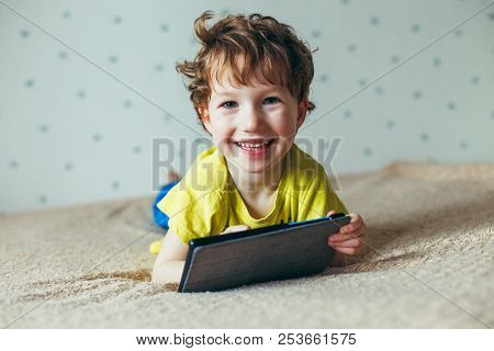 Happy Toddler Boy Having Fun Playing Game On Gadget , Preschool Kid Sititng On Sofa With Smiling Fac