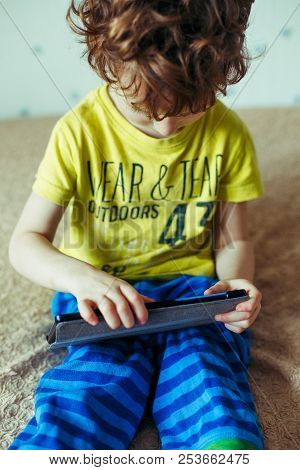 Little Cute Boy In A Green T-shirt Playing Games On A Tablet And Watching Cartoons. Addiction Concep