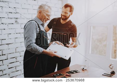 Workers Checking Laptop In Hands In Repair Shop. Worker With Tools. Computer Hardware. Young And Old