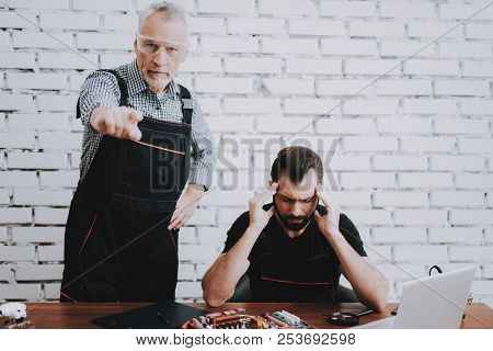 Angry Elderly Man Pointing Finger At Screen. Upset Young Man Sitting At Table. Young And Old Workers