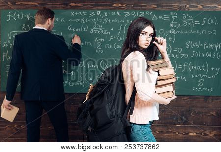 Preparation To Exam. Woman Student Look In Glasses With Book Stack And Backpack With Teacher Man Wri