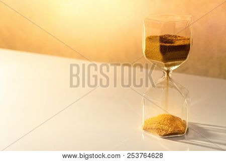 Gold Sand Running Through The Shape Of Modern Hourglass On White Table.time Passing And Running Out 