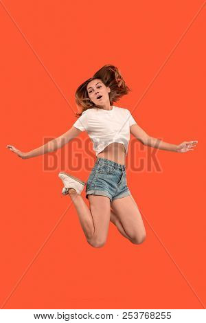 Freedom In Moving. Mid-air Shot Of Pretty Happy Young Woman Jumping And Gesturing Against Orange Stu