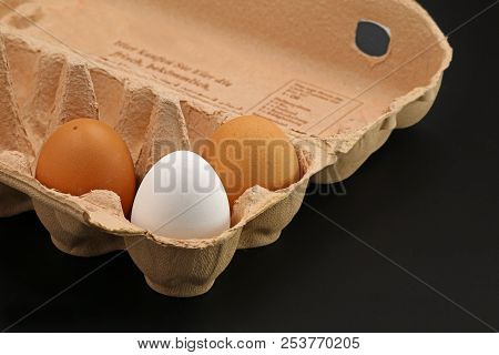 Three Brown Eggs In A Grey Cardboard Box On Black Background