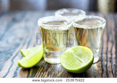 Three Glasses Of Tequila And Limes In A Defocus On A Blurred Background