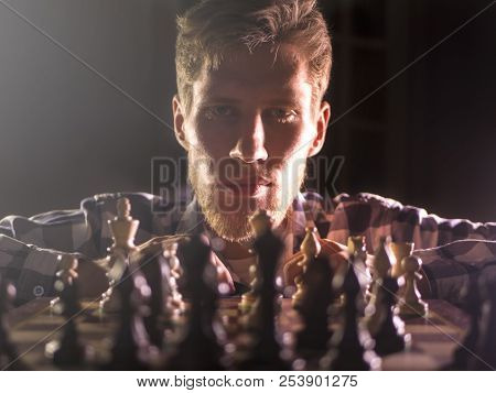 Young Bearded Chess Grandmaster Sitting And Thinking On The Next Move In Dark Room