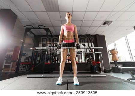 Sexy Woman With A Ponytale Wearing Pink And Black Professional Sportswear Squatting With An Iron Bar