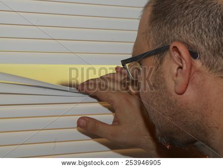 A Man Presses The Rails Blinds And Looks Out The Window.
