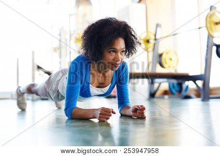 Confident fit African-American woman looking forward while standing in plank position training abs