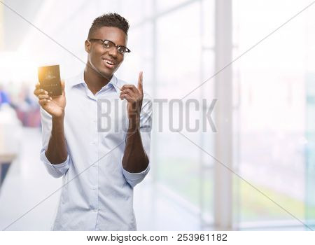 Young african american man holding australian passport surprised with an idea or question pointing finger with happy face, number one