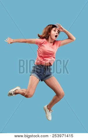 Freedom In Moving. Mid-air Shot Of Pretty Happy Surprised Young Woman Jumping Against Blue Studio Ba