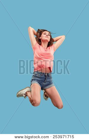 Freedom In Moving. Mid-air Shot Of Pretty Happy Young Woman Jumping And Gesturing Against Blue Studi