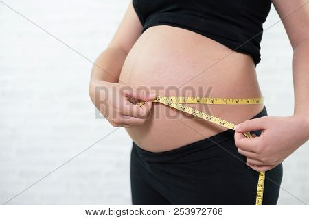 Pregnant Woman Measures Belly Circumference Isolated On Gray Background