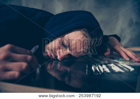 Frustrated Exhausted Bearded Guy In Black Dark Clothing Lying On Glass Table Near Cocalines After Sn