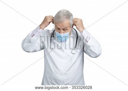 Old Doctor Put On Medical Mask. Physicial Wearing Protective Mask. White Isolated Background.