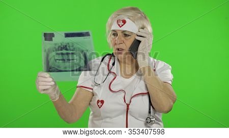 Portrait Of Elderly Caucasian Female Doctor Talking On The Phone With Client. Female Nurse With Radi