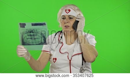 Portrait Of Elderly Caucasian Female Doctor Talking On The Phone With Client. Female Nurse With Radi