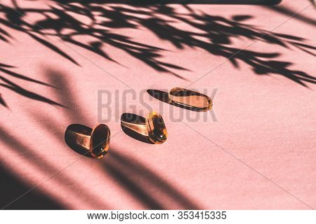 Oil Yellow Gelatin Capsules On Pink Background With Flower Shadow, Vitamins And Antioxidant Concept 