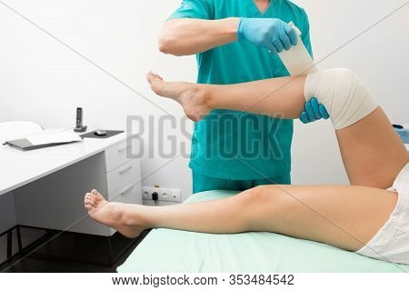 Traumatologist Bandaging Damaged Knee Of A Woman With An Elastic Bandage. Physiotherapist Bandaging 