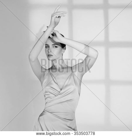 Woman in elegant fashionable dress. Beautiful model pose in studio in evening clothes. Classic silk dress. Sexy lady stay on white background. Perfect young woman with classic hairstyle and makeup. 
