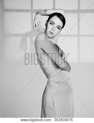 Woman in elegant fashionable dress. Beautiful model pose in studio in evening clothes. Classic silk dress. Sexy lady stay on white background. Perfect young woman with classic hairstyle and makeup. 