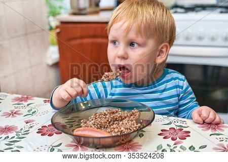 Three-year-old With Red Hair And Light Eyes Holding A Spoonful Of Porridge From His Open Mouth