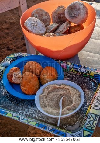 African street food, fried bread and traditional fatcakes, doughnuts, with a bowl of brown sugar