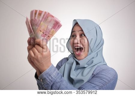 Portrait Of Indonesian Muslim Woman Holding Rupiah Money, Smiling Laughing Winning Gesture