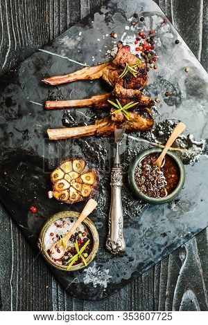 Grilling Lamb Chops On Meat Fork With With Salt, Pepper On Dark Stone Plate On Black Old Rustic Wood
