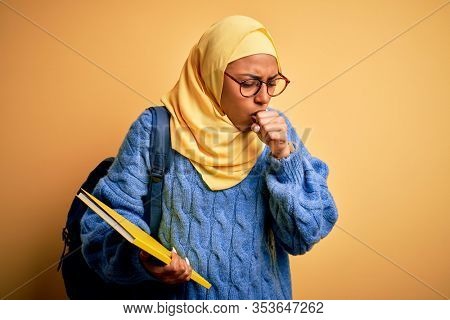 Young African American student woman wearing muslim hijab and backpack holding book feeling unwell and coughing as symptom for cold or bronchitis. Health care concept.