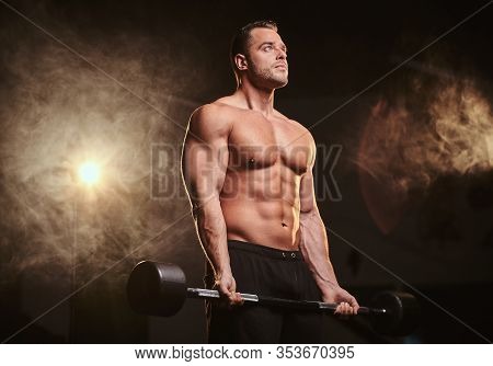 Fit Mucular Bodybuilder Doing Weightlifts With Barbell In A Dark Gym Surrounded By Smoke