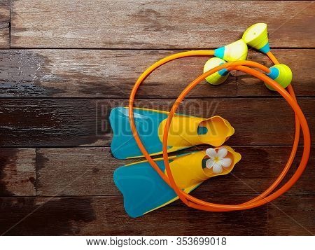 Pair Of Blue And Yellow Flippers And Toy Swimming Aid For Children Diving Practice On Wet Wooden Flo